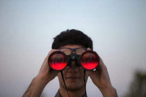 Homme observant à travers des jumelles rouges – illustration des signaux d’alerte liés aux risques psychosociaux