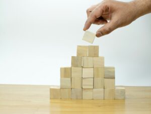 Main plaçant un cube au sommet d’une pyramide en bois, illustrant l’accompagnement du plan d’action DUERP